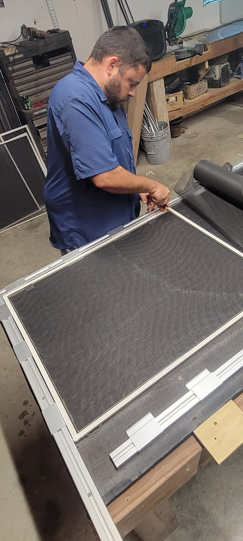 A man working on a screen. He is using a tool on a screen frame in a workshop.