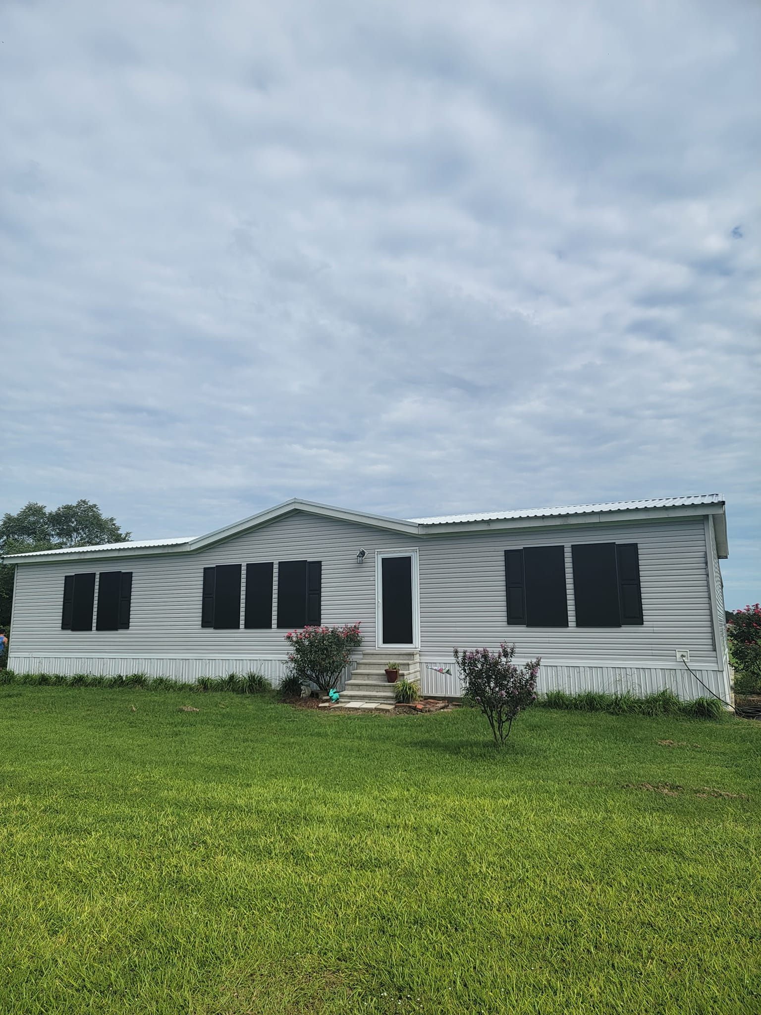 Mobile home with light siding, black window screens, and green lawn under cloudy sky.