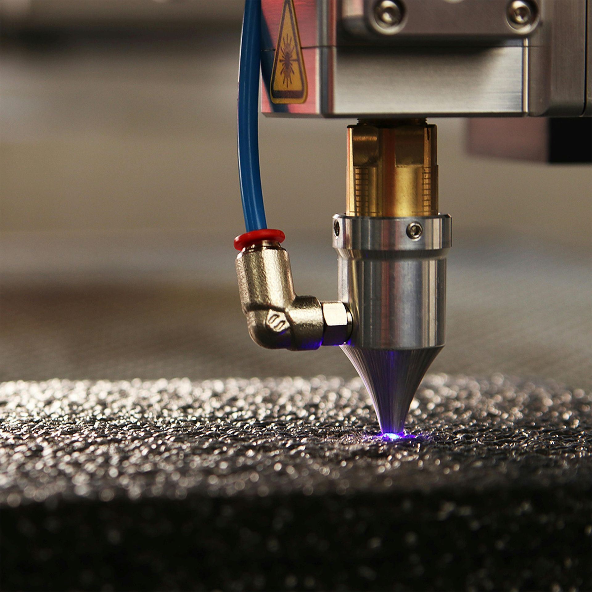 Laser cutting nozzle emitting a purple beam onto a textured metal surface