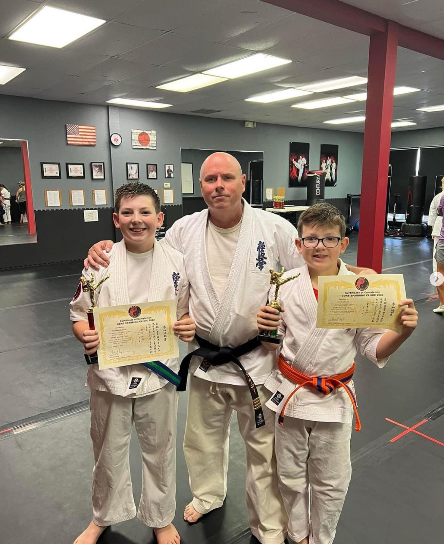 A man and two young boys are standing next to each other in a gym holding trophies.