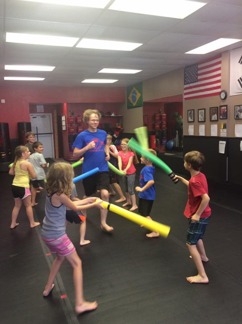A group of children are playing with foam sticks in a gym