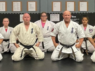 A group of people in karate uniforms are kneeling on the floor.