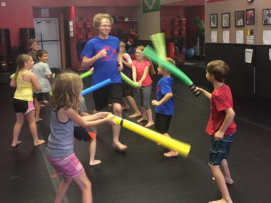 A group of children are playing with foam swords in a gym