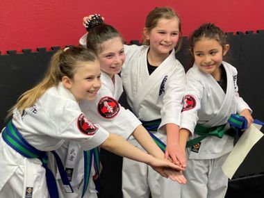 A group of young girls in karate uniforms are putting their hands together.
