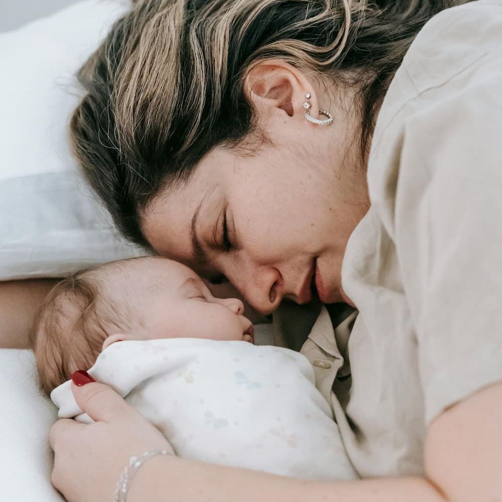 A woman is laying on a bed holding a baby wrapped in a blanket.