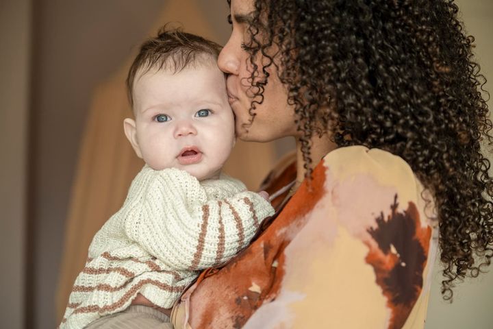 A woman is holding a baby in her arms and kissing it on the cheek.