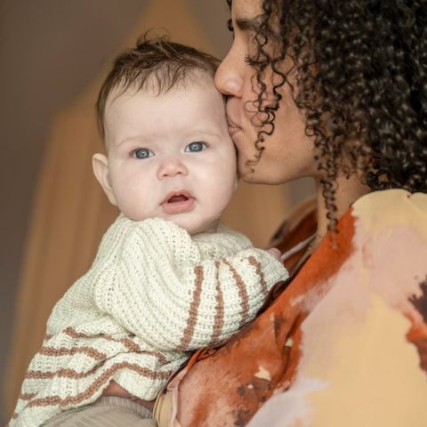 A new mom is kissing a new baby on the cheek