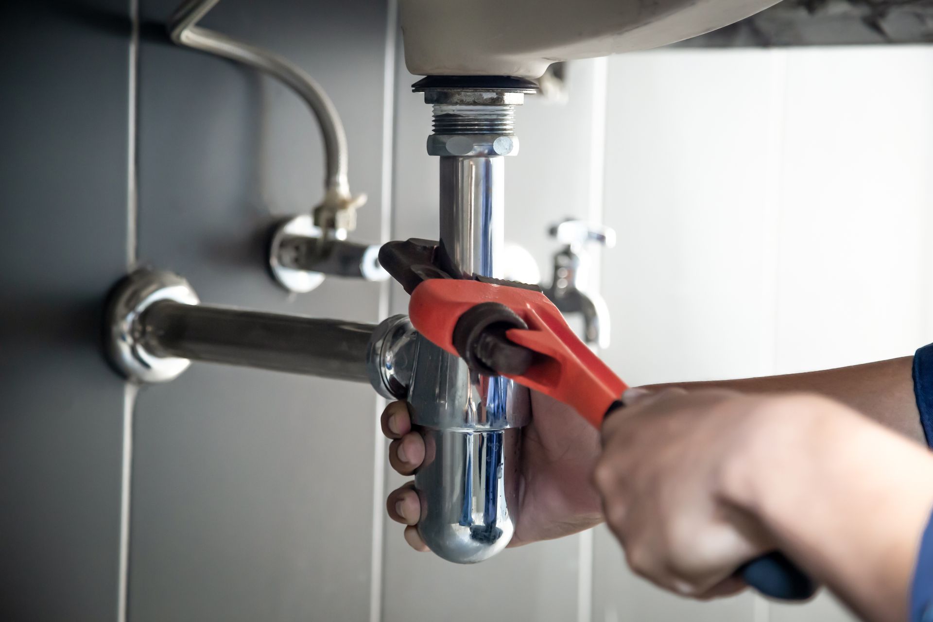 A plumber is fixing a sink pipe with a wrench.