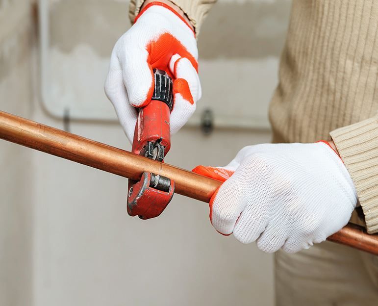 A person is cutting a copper pipe with a pipe cutter.