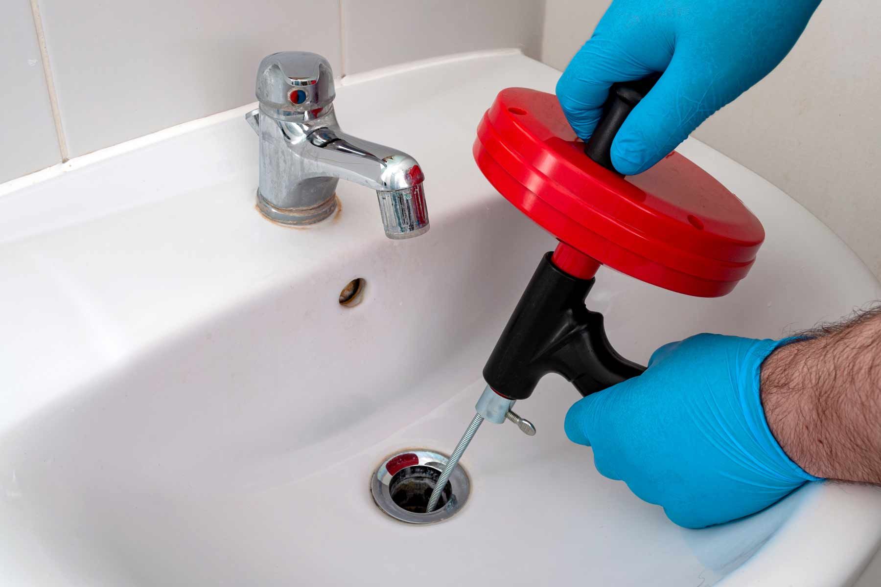 A person is using a drain snake to unblock a sink.