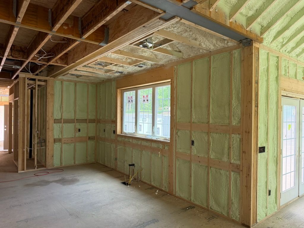 Unfinished room with exposed framing, green insulation panels, and a window cutout under construction.