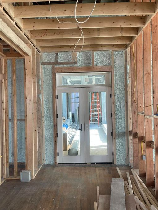 Unfinished room framed with exposed wood studs, leading to a doorway and bright construction area beyond.