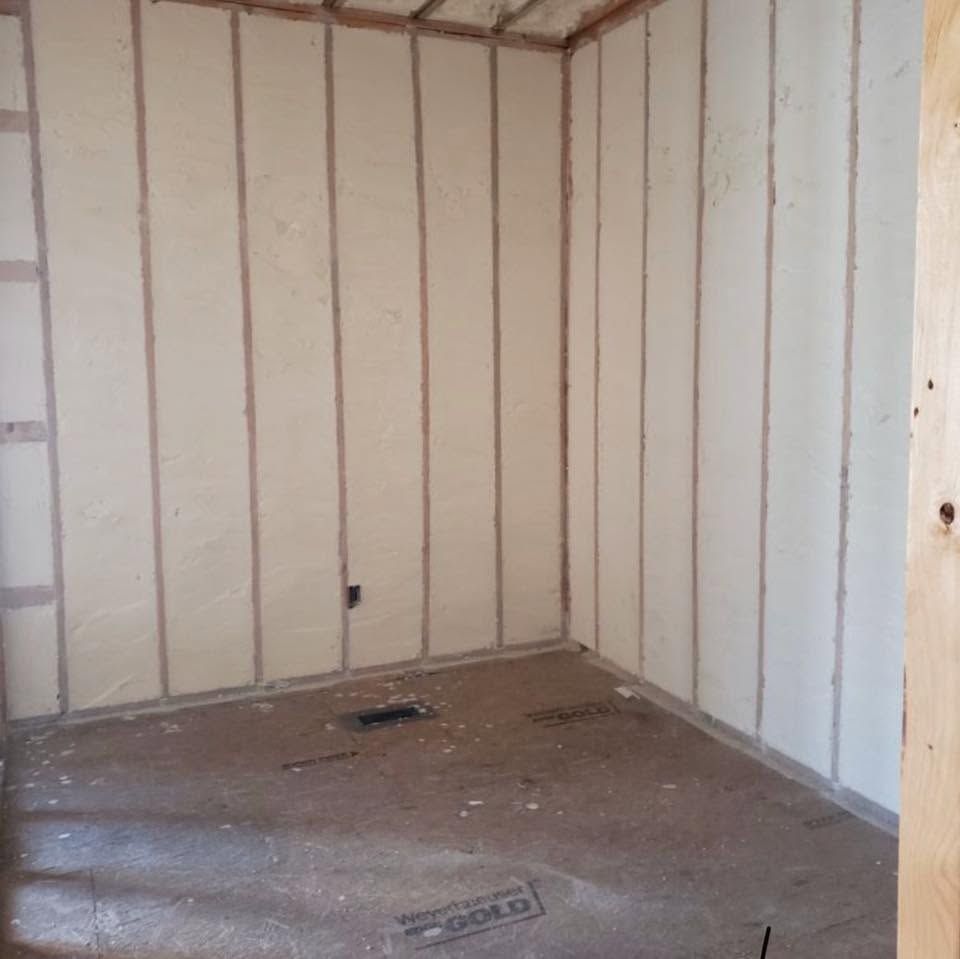 Empty unfinished room with white wall panels, exposed framing, and a bare floor.