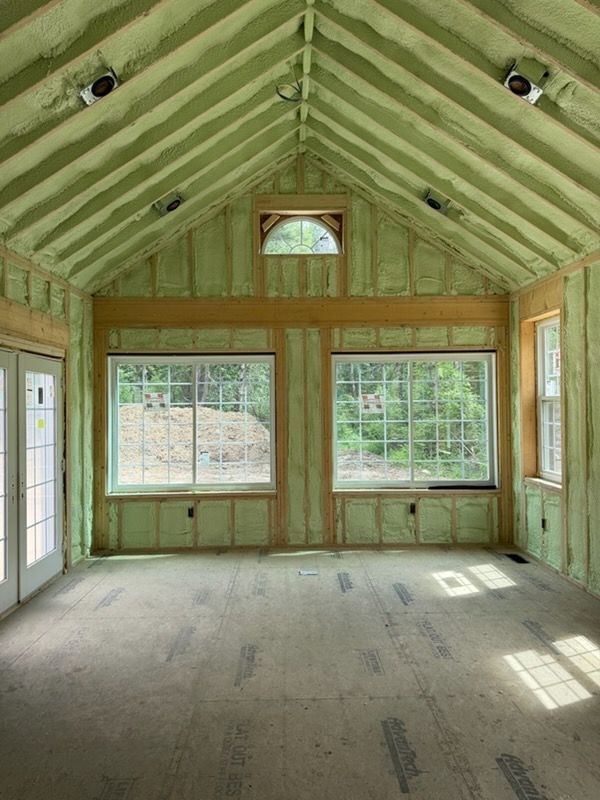 Empty unfinished room with green insulation, exposed wooden framing, and large windows at the far end