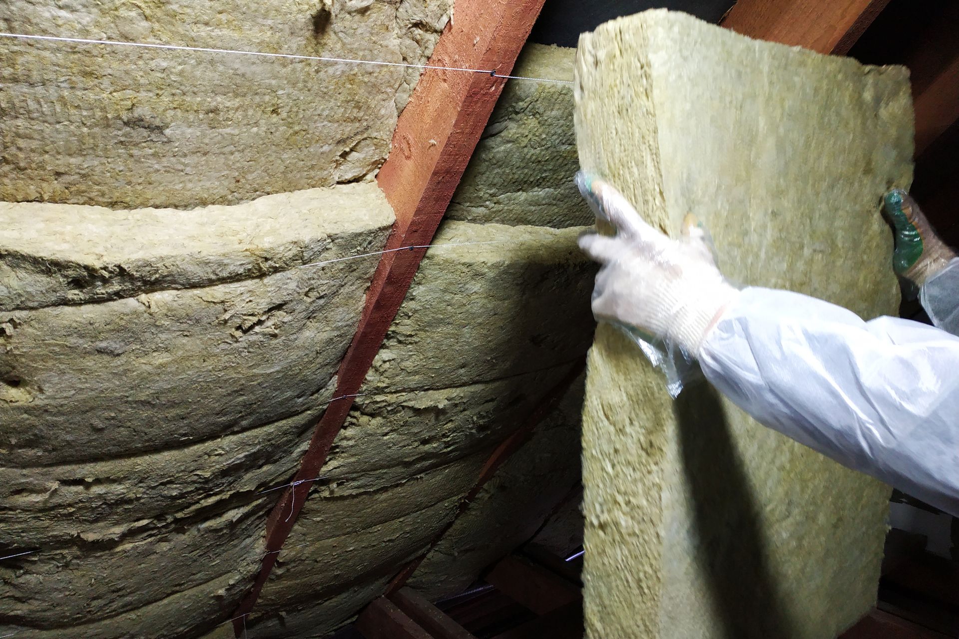 Person in white gloves inspecting insulation between roof rafters