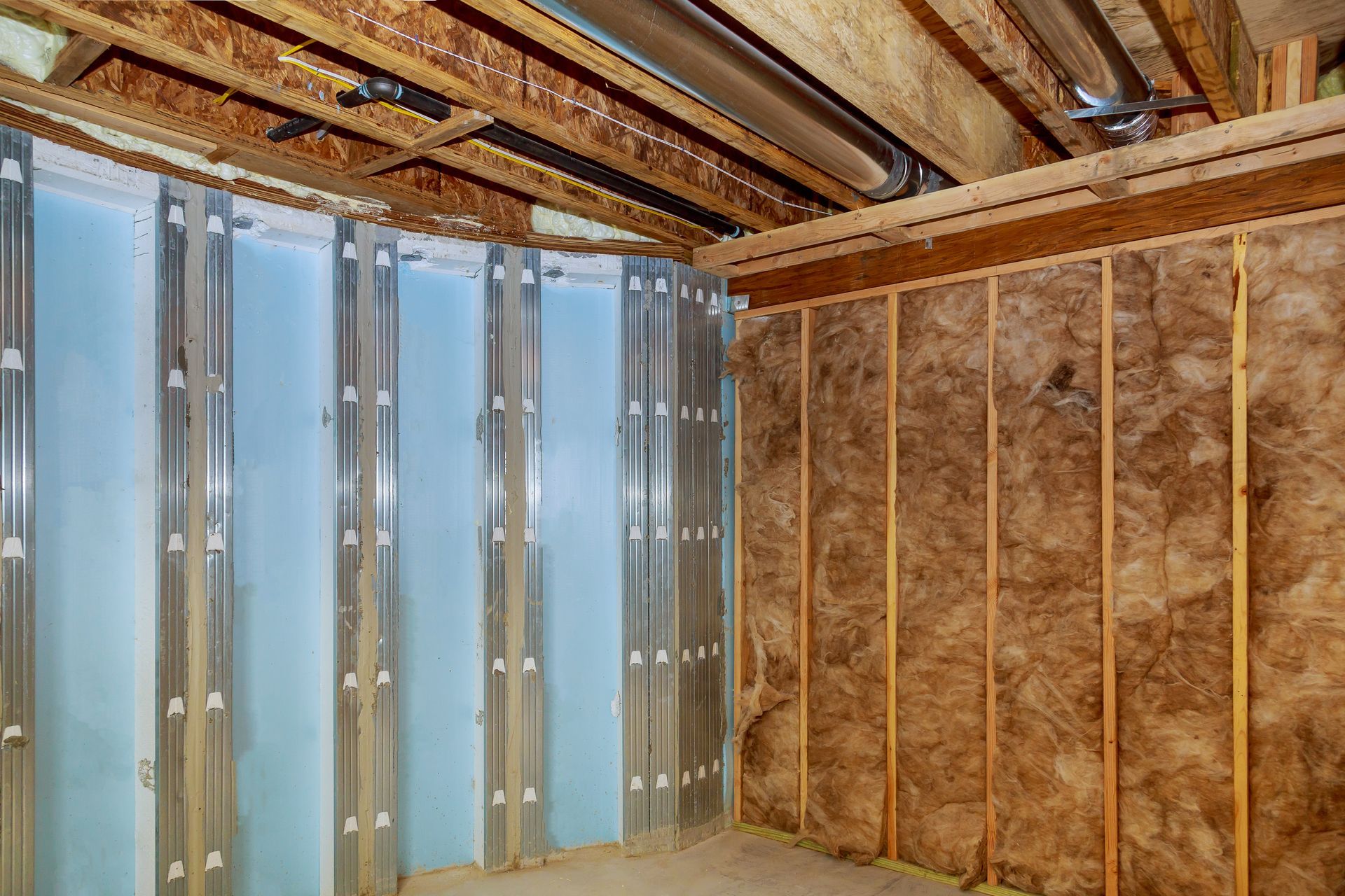 Unfinished basement with exposed insulation, metal studs, and wooden ceiling joists