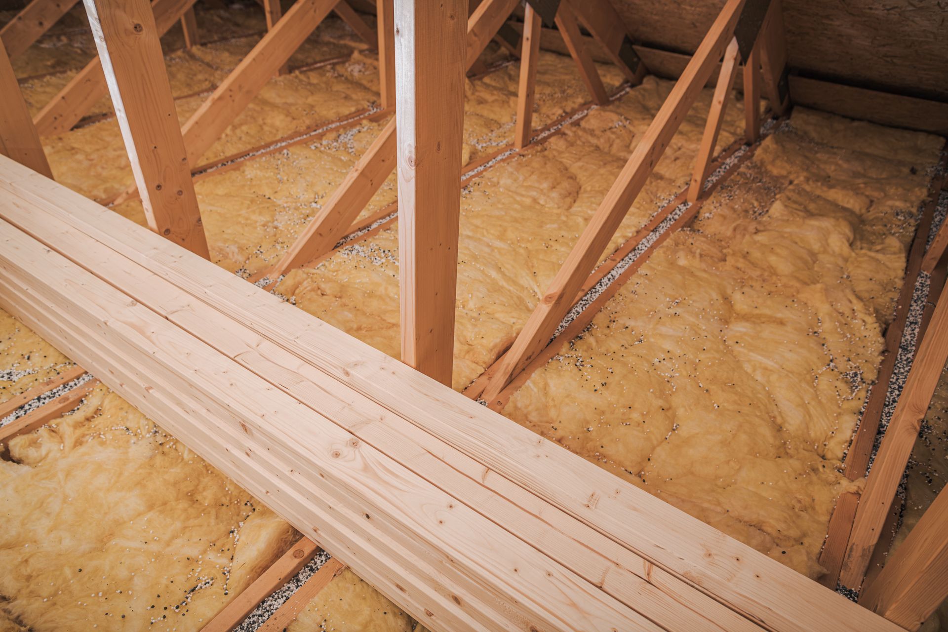 Stacked lumber and wooden joists in an unfinished attic with exposed insulation and framing