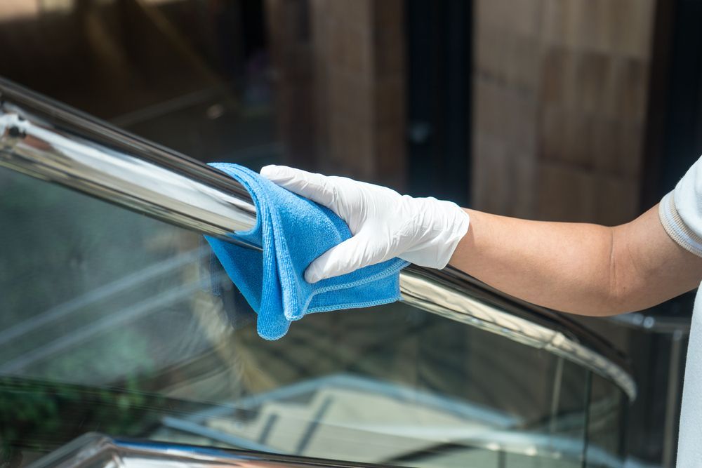 A person wearing a white glove wipes a shiny metal railing with a blue microfiber cloth.