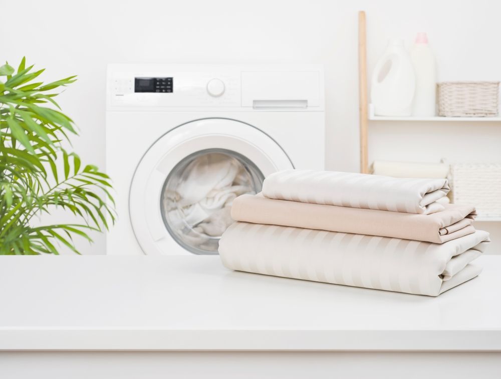 A clean laundry room featuring a white washing machine, a stack of folded pastel linens, and a potted plant on a counter.