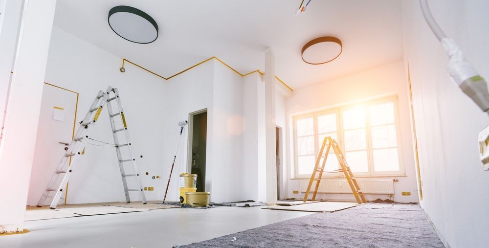 Two stepladders stand in a bright, sunlit room under construction with white walls and circular ceiling lights.