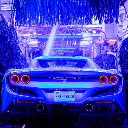 Blue sports car in a neon-lit car wash, rear view with glowing taillights.