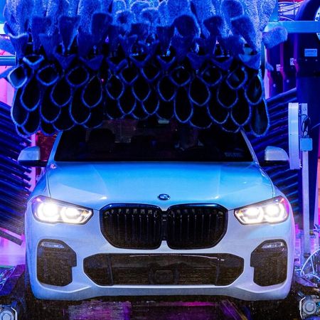White BMW under a stack of blue tires in a neon-lit garage
