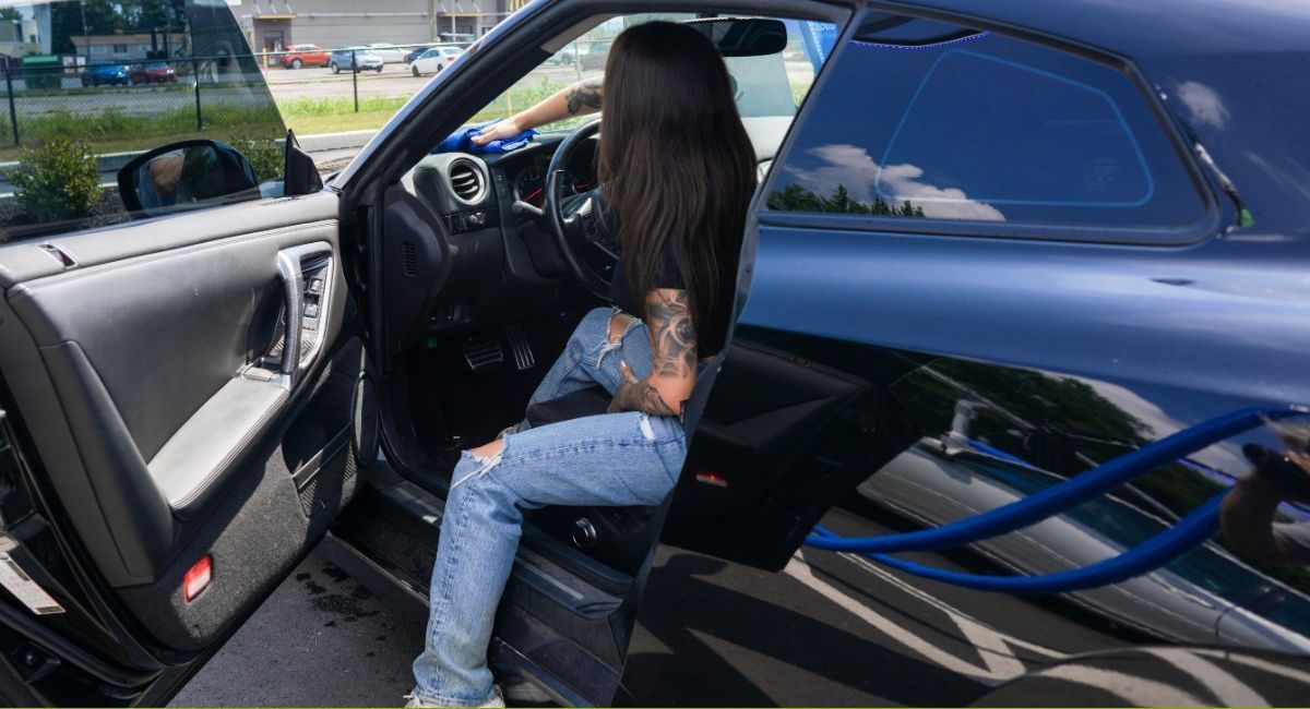 Person seated in a dark blue car with the door open, viewed from the side.