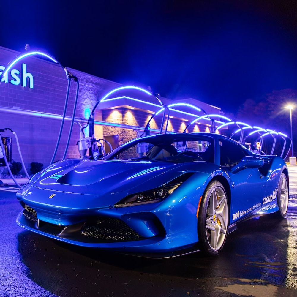 Blue sports car parked at night under purple neon lights outside a modern building