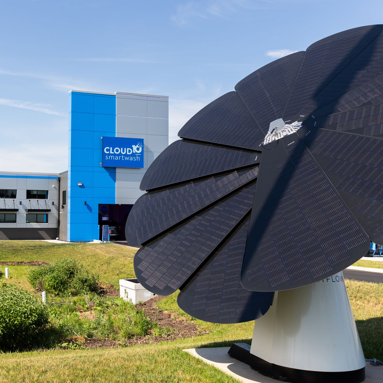 Large black satellite dish sculpture in front of a blue building on a sunny lawn