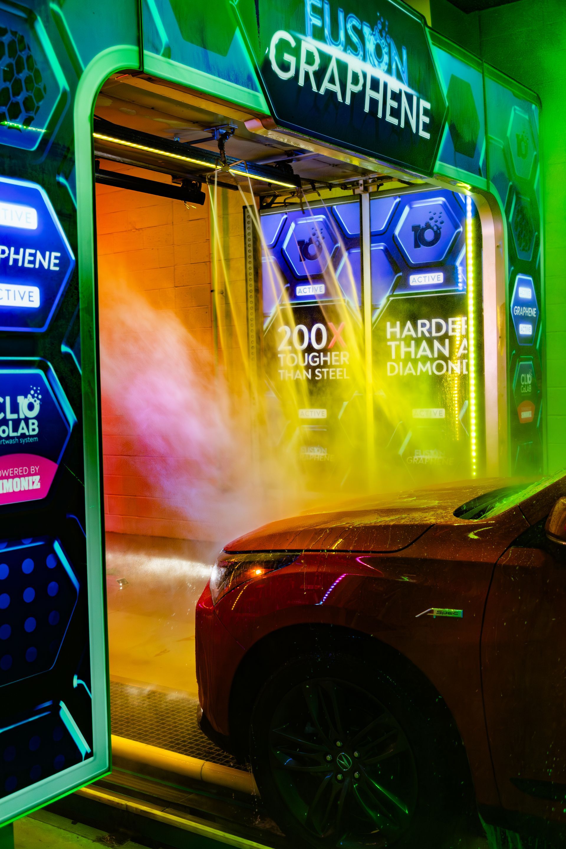 Red sports car beside a bright neon car wash with green and blue signage.