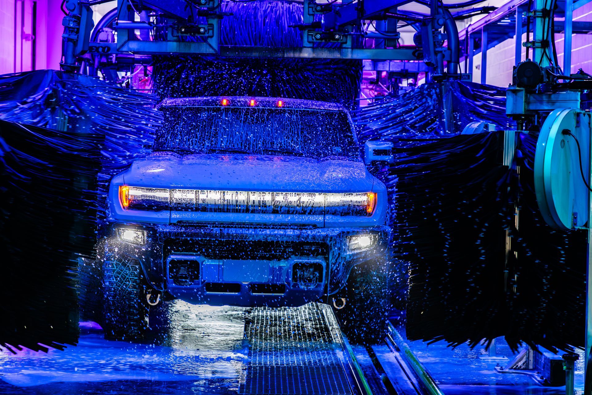 Blue vehicle being washed in an automated car wash under bright neon lights