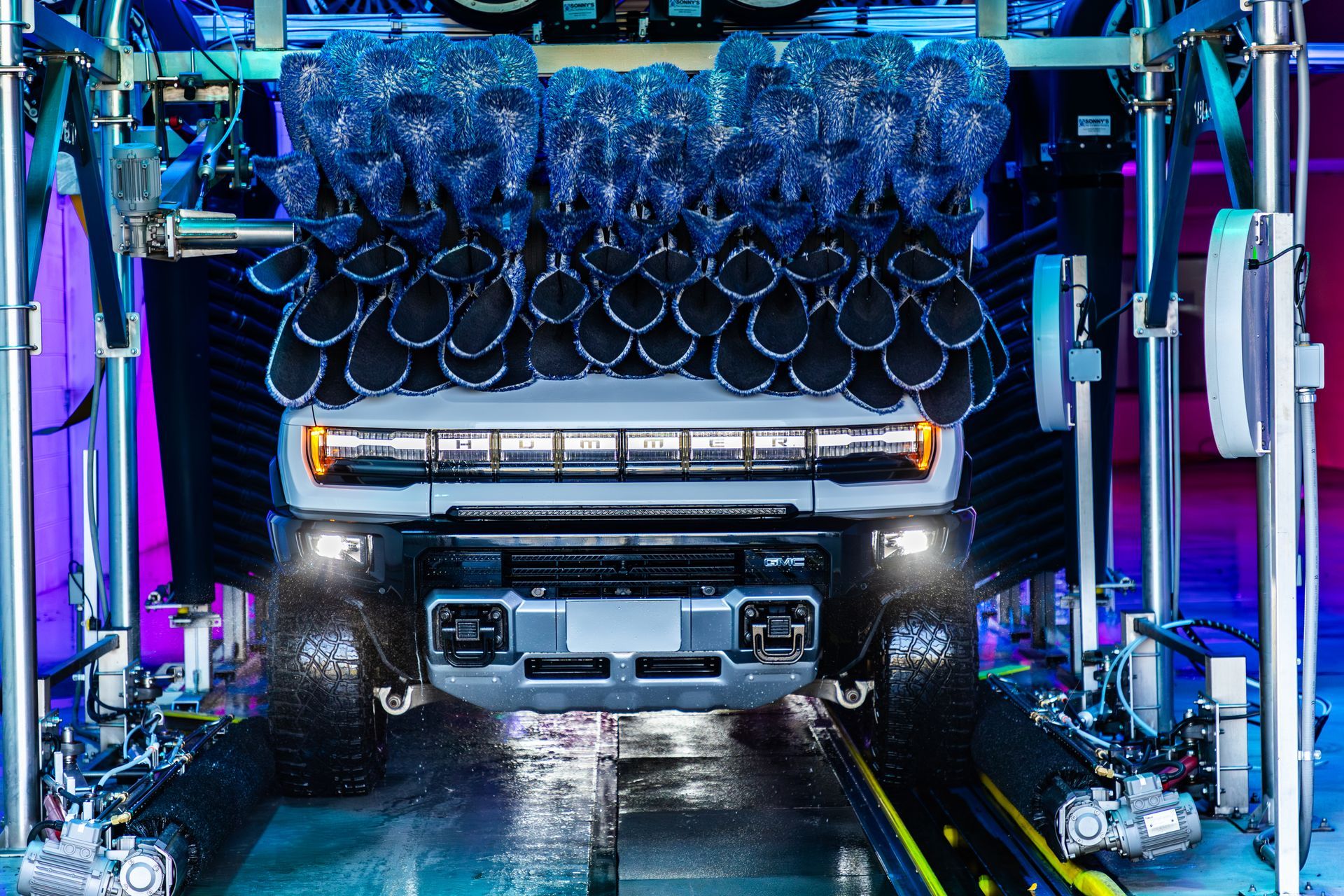 Jeep in blue-lit car wash with foamy water spraying over it