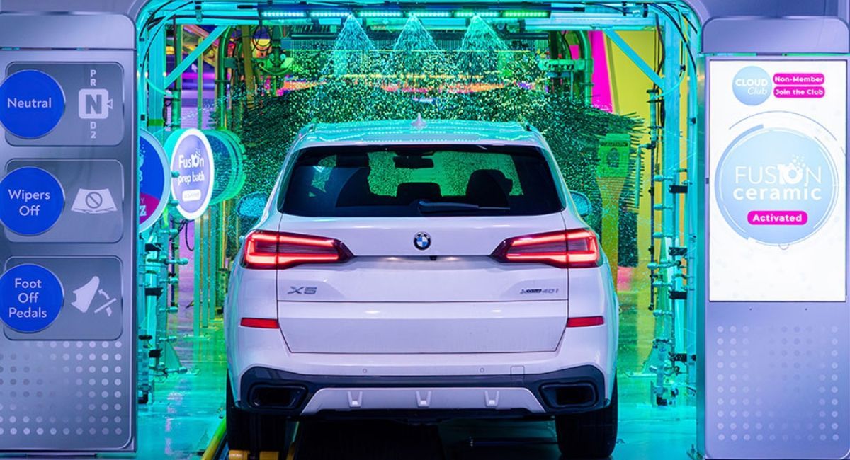White SUV in a colorful car wash tunnel with water and foam spraying around it