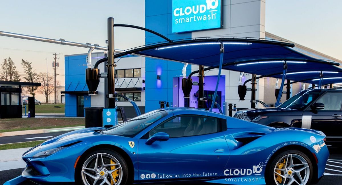 Blue Ferrari sports car on display at an outdoor event beside a charging station