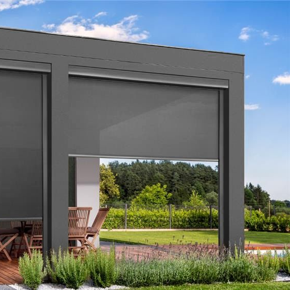 A patio with dark grey outdoor roller shades, one fully lowered and one partially lowered, overlooking a green backyard.