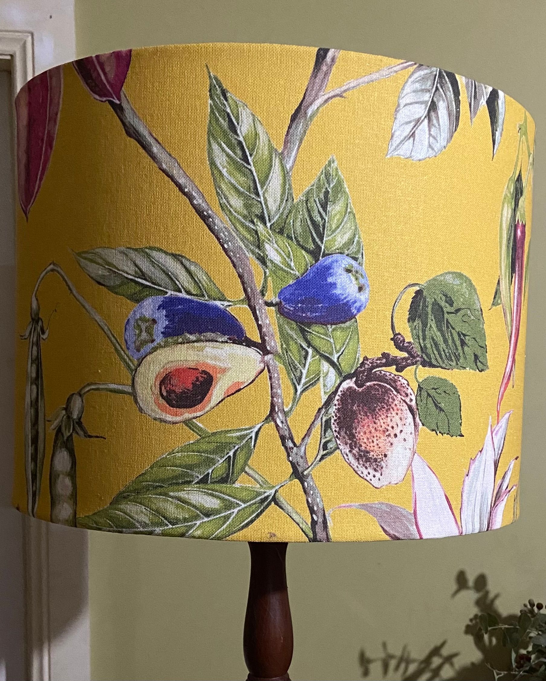 A yellow lamp shade featuring a botanical print of leaves, berries, and a sliced avocado on thin, dark branches.