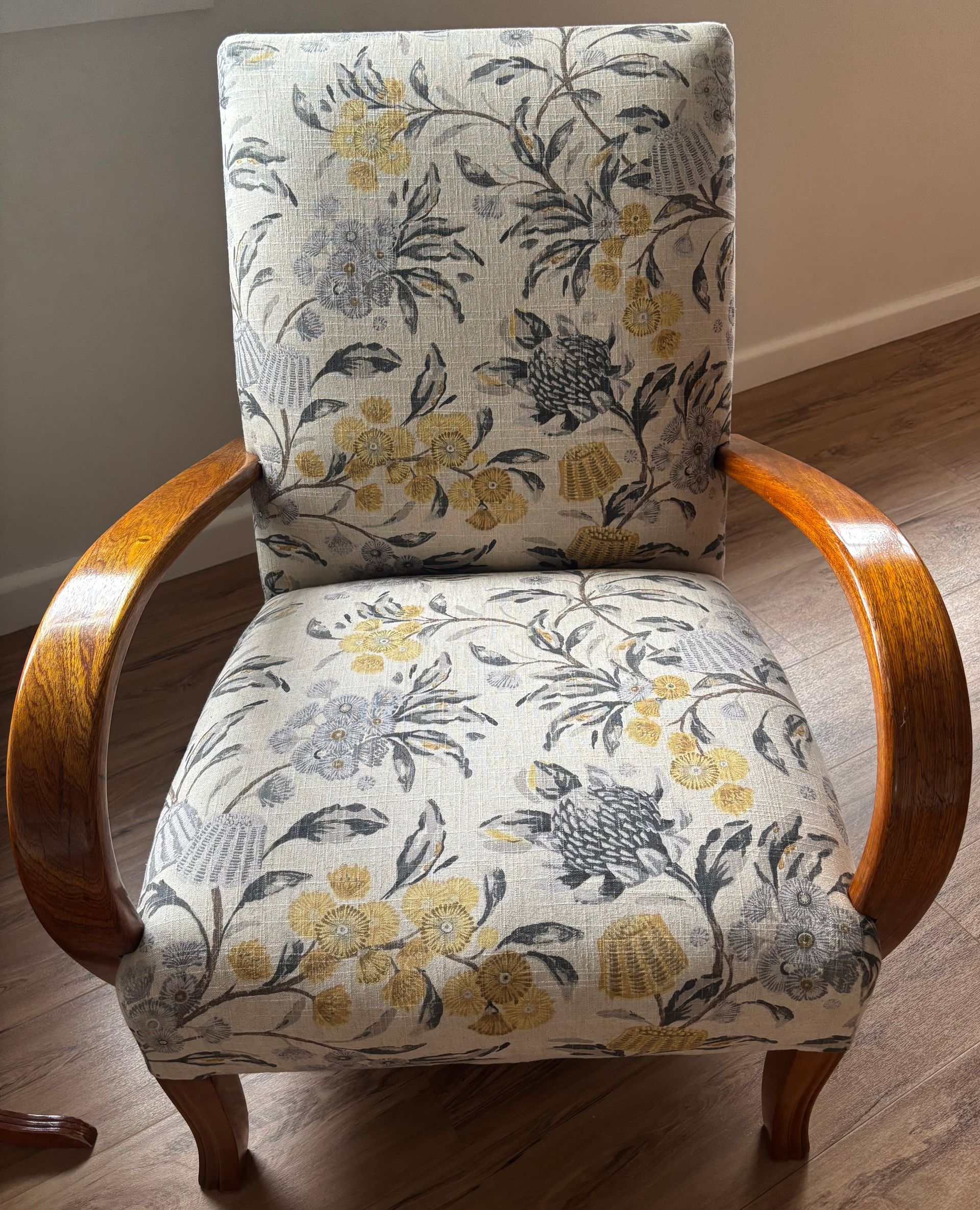 A cushioned armchair featuring curved wooden arms and a cream fabric upholstery with a yellow and gray floral print.