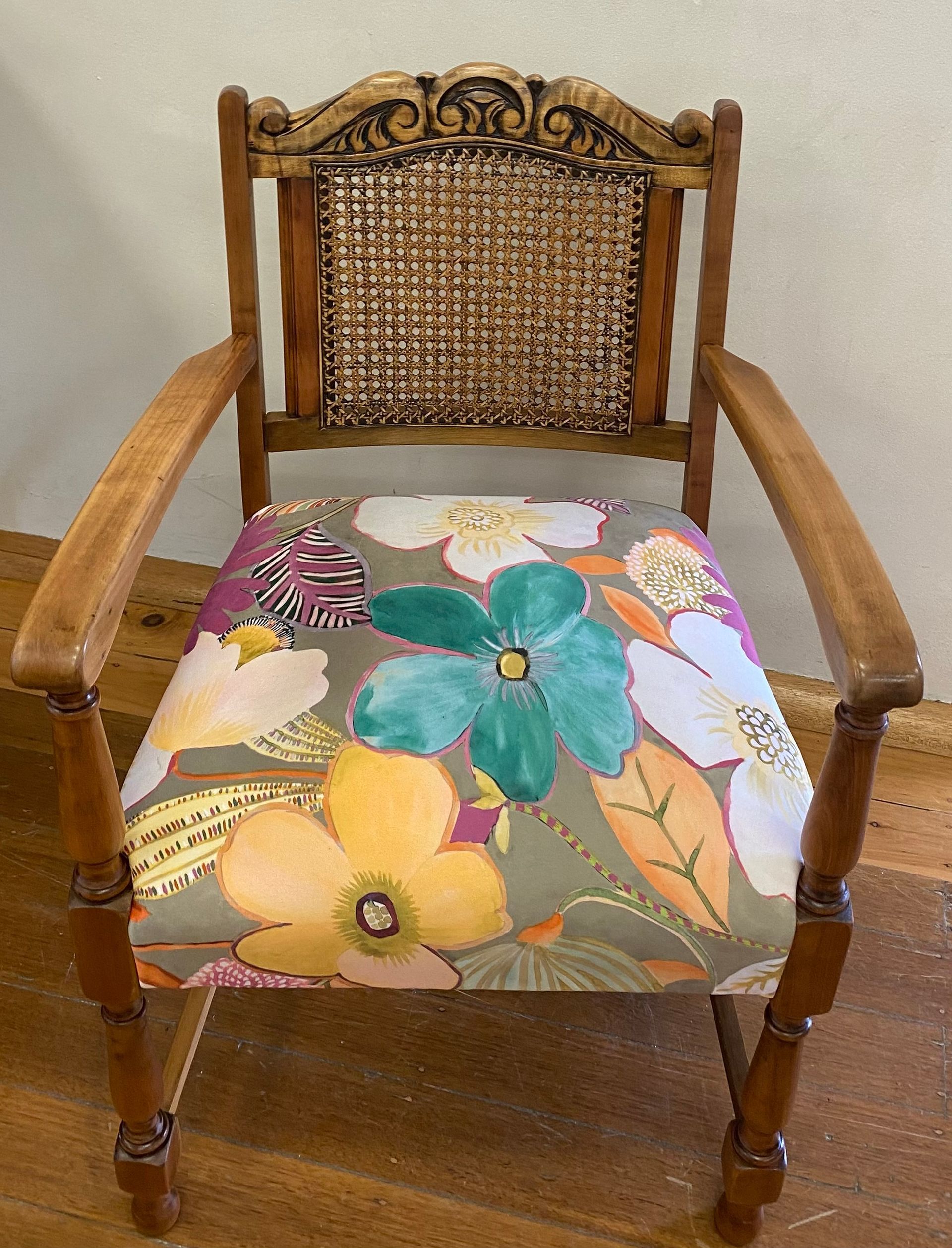 A wooden armchair with a cane back, carved top rail, and a seat upholstered in a bold, colorful floral fabric.