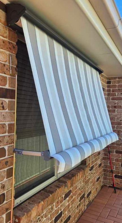 A grey and white striped window awning extended over a brick wall window.
