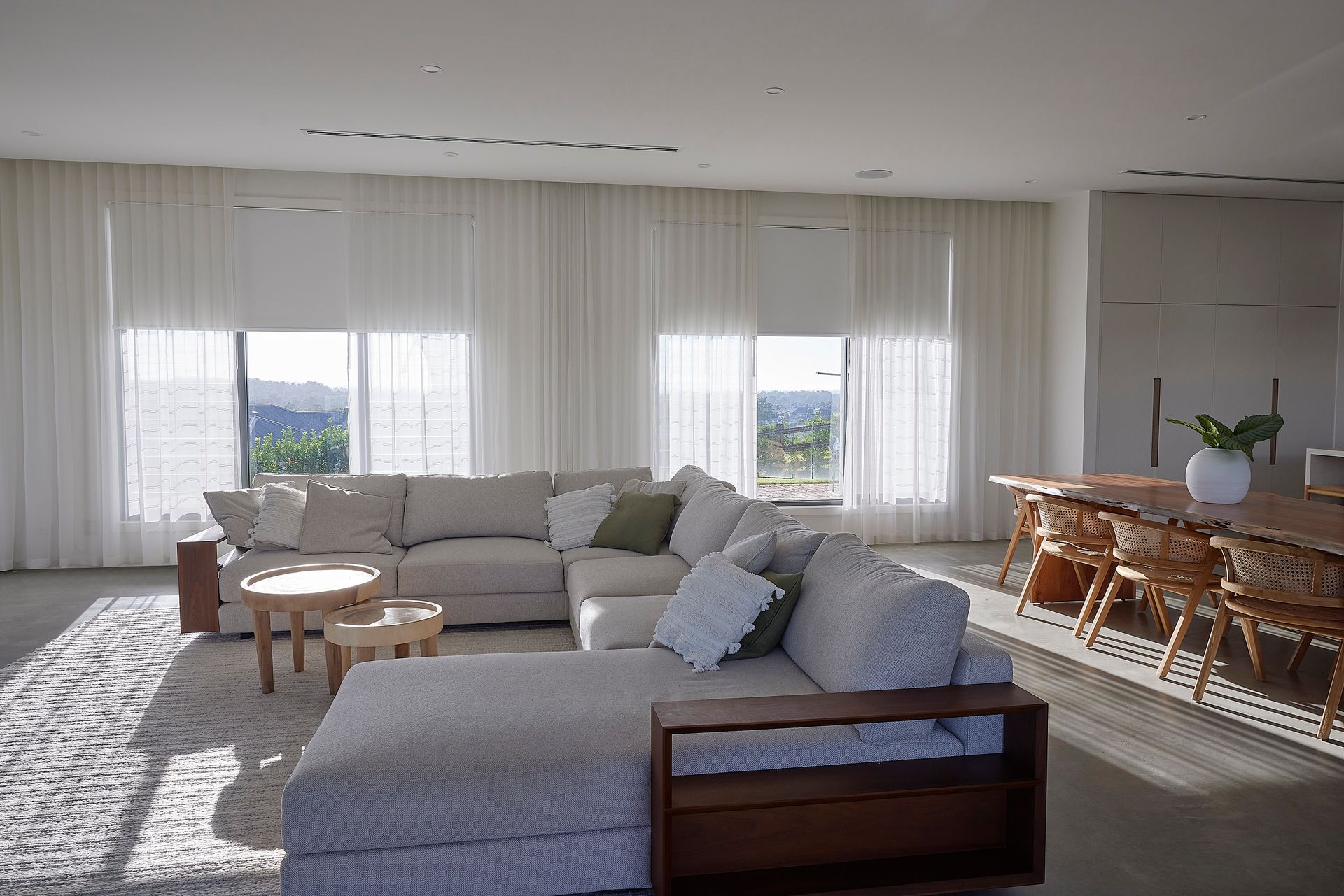 Sunlit living room with sectional sofa, sheer curtains, and wooden table setting.
