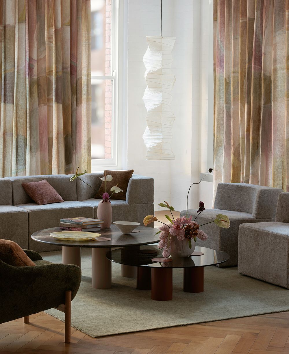 Modern living room with a gray sectional, two glass coffee tables, a neutral rug, and vertical striped curtains.