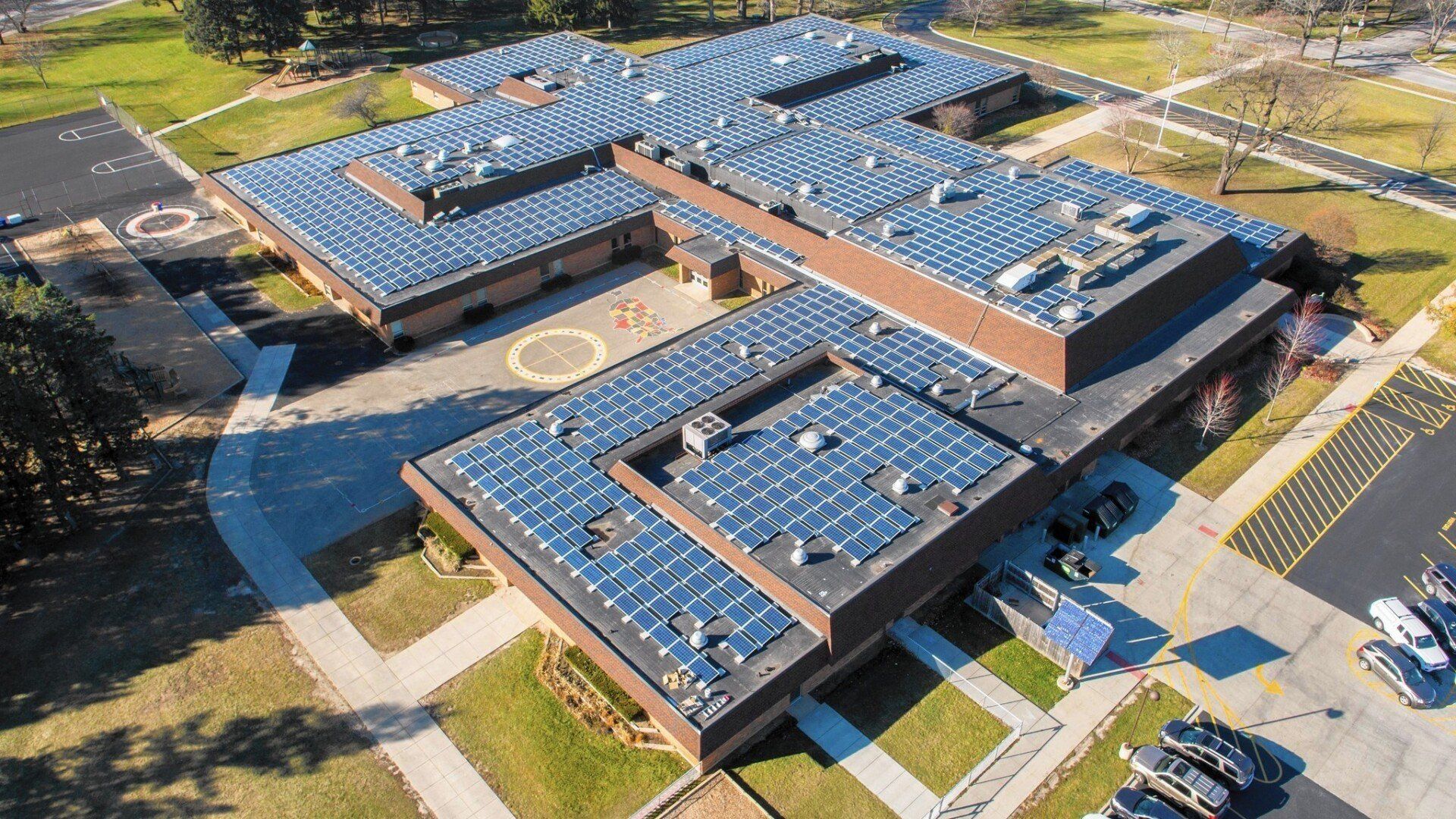 Aerial view of a modern school campus with blue solar panels on multiple rooftops and parking lots nearby
