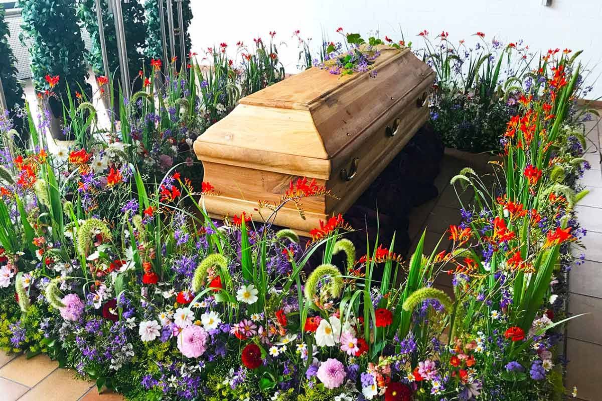 Ein Holzsarg ist auf einem Friedhof von Blumen umgeben.