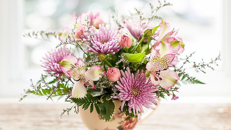 Auf einem Tisch steht eine Vase mit rosa und weißen Blumen.