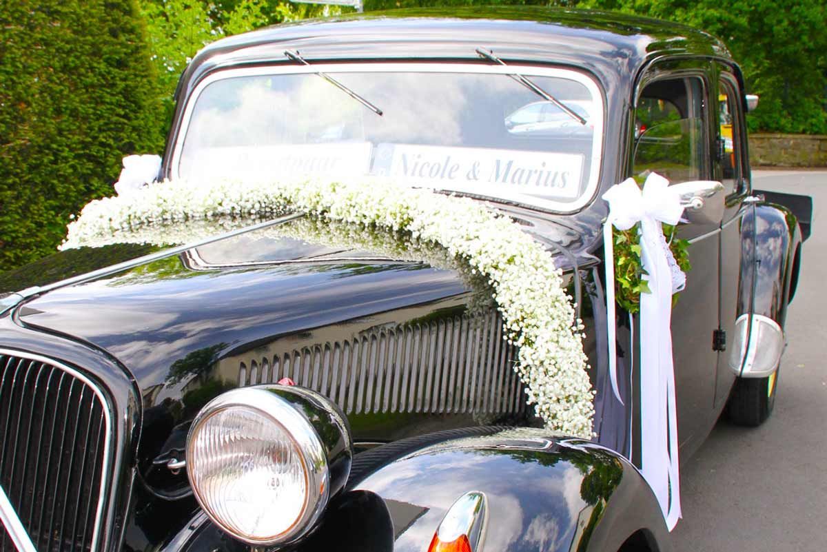 Ein schwarzes Auto ist mit weißen Blumen und Bändern für eine Hochzeit geschmückt