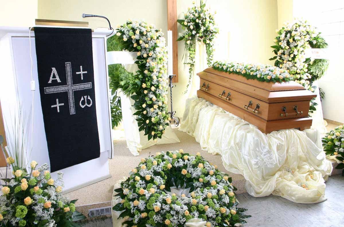 Ein Sarg steht auf einem Tisch in einer Kirche, umgeben von Blumen.