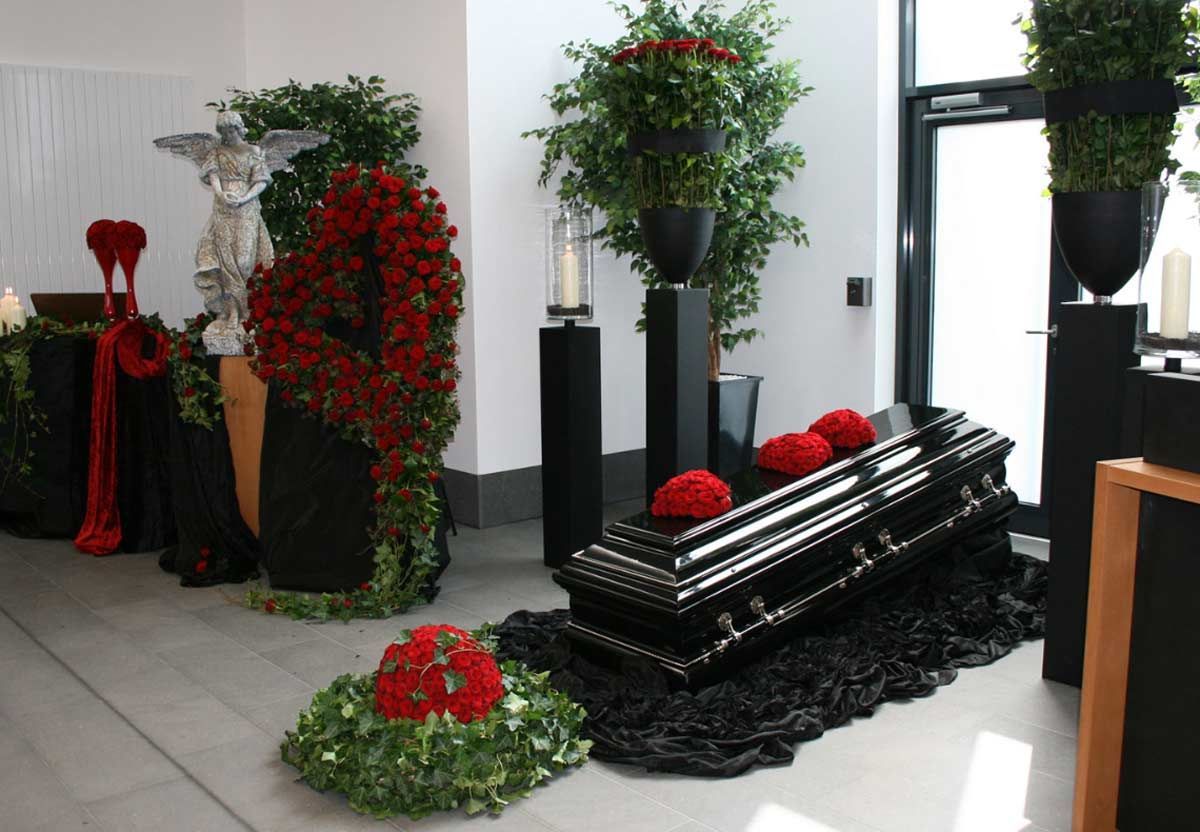 Ein schwarzer Sarg steht in einem mit Blumen geschmückten Raum