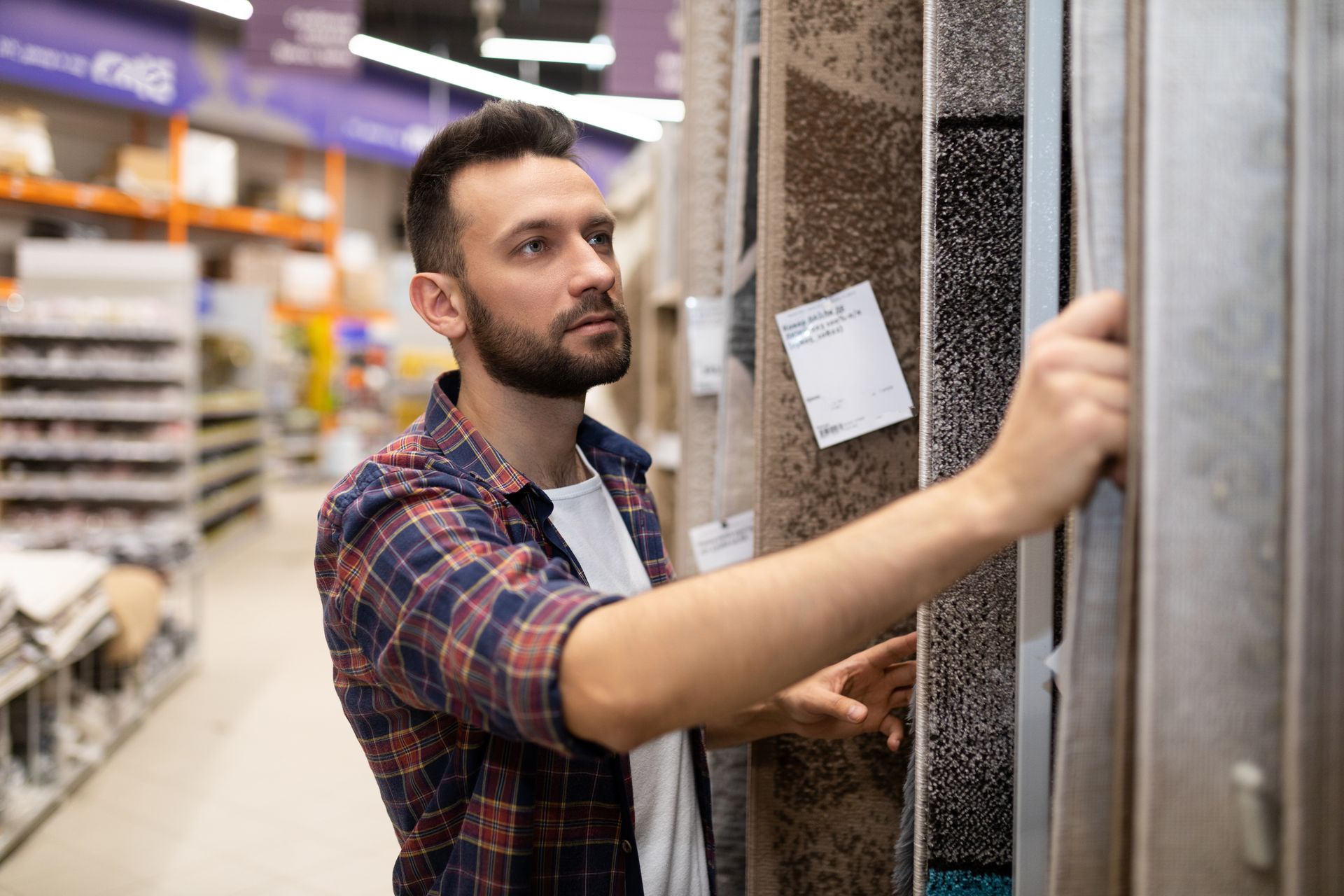 Man browsing carpet samples in a home improvement store aisle.