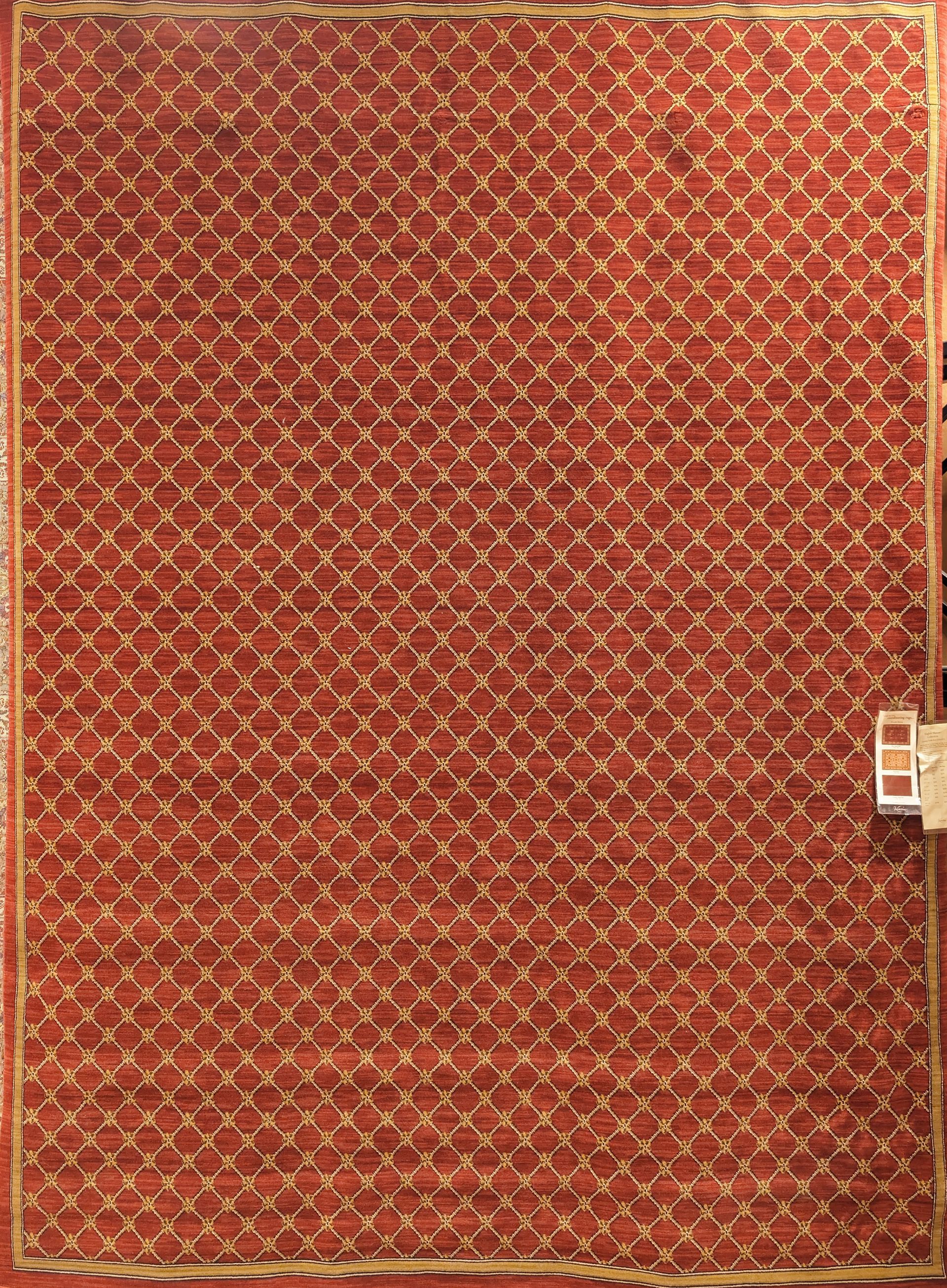 Red patterned carpet or rug with a beige border and a small white tag on the right edge