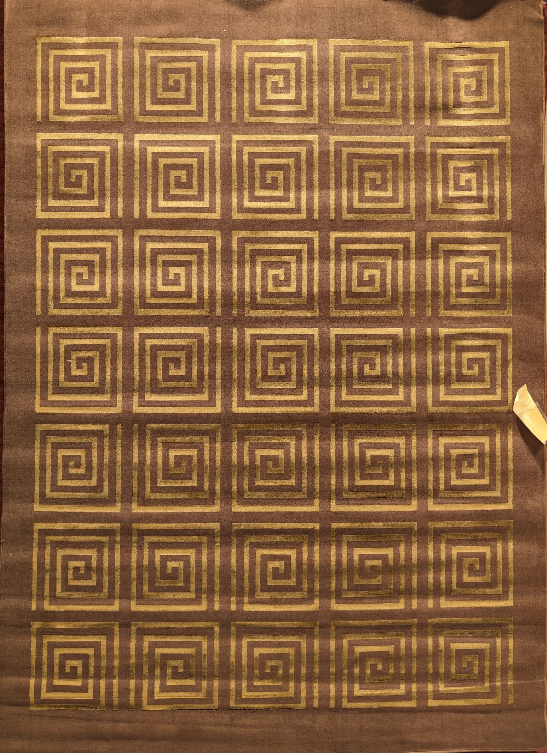 Brown woven rug with a repeating gold geometric maze pattern